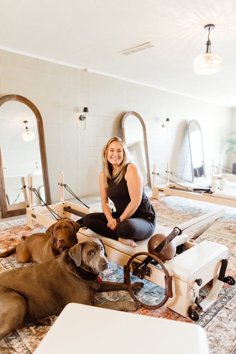 Jamie sitting on a reformer with her two chocolate Labs