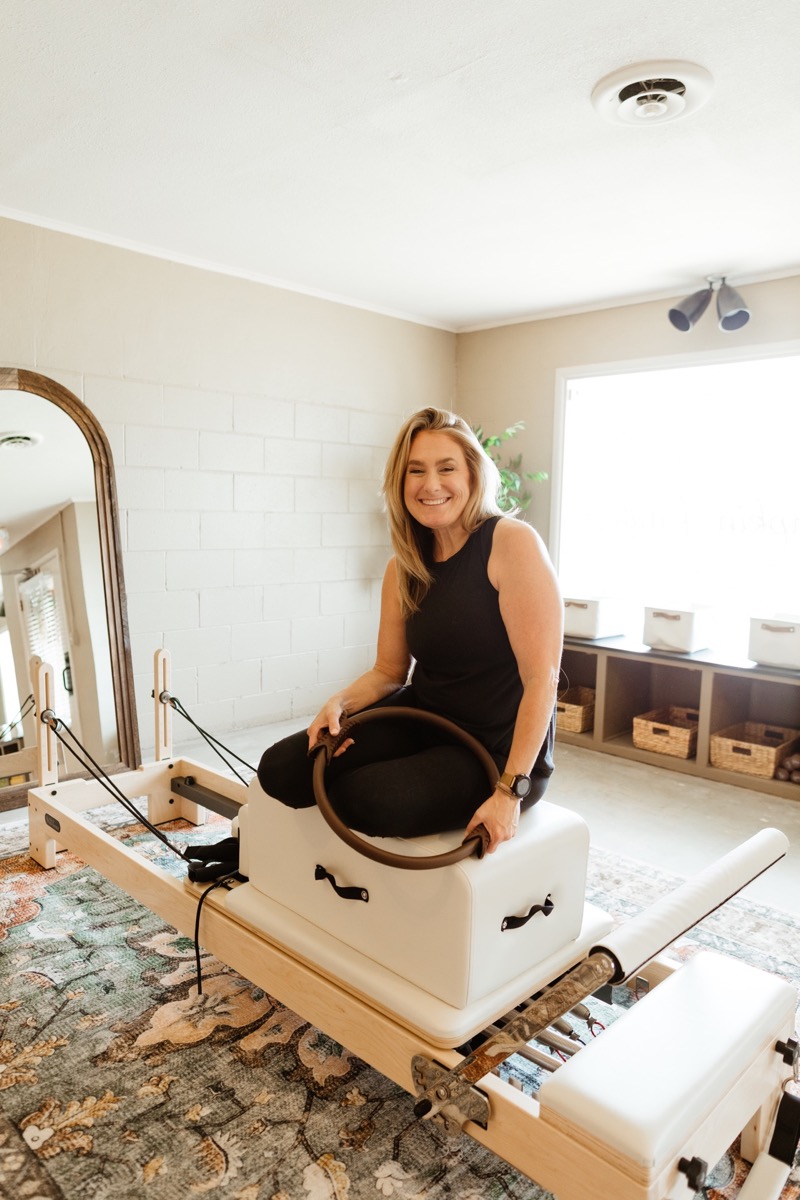Jamie smiling on a reformer box with a Pilates ring